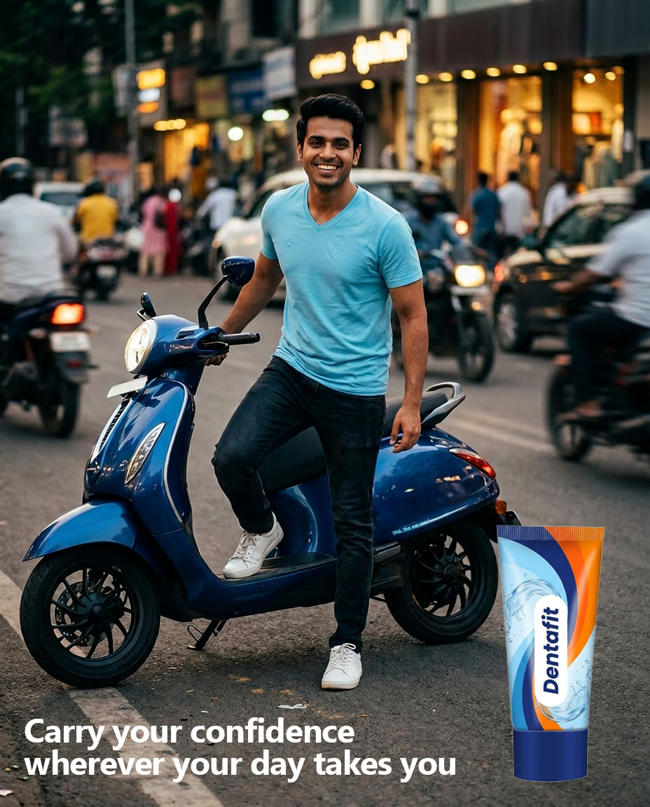 Smiling man in a blue T‑shirt sits on a blue scooter on a busy street; a Dentafit toothpaste tube stands beside him, conveying brand confidence on the go.